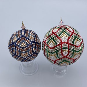 Puede incluir: Dos adornos navideños de cuentas en soportes transparentes. El adorno de la izquierda es azul, marrón y blanco. El adorno de la derecha es rojo, verde, dorado y blanco.