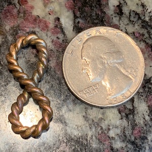 May include: A gold-colored infinity symbol charm made of twisted wire. The charm is about the size of a US quarter.