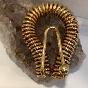 May include: A gold-colored metal spring coil clasp with a hook closure. The clasp is made of multiple small coils that are connected together.