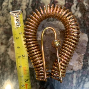 May include: A gold-colored metal spring coil with a hook and a ball at the end. The spring coil is about 6 inches in diameter.