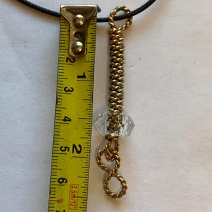 May include: A handmade pendant necklace featuring a gold-colored metal spring design with a clear, faceted crystal bead. The pendant is approximately 3 inches (7.6 cm) long and hangs from a black cord.