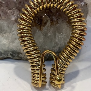 May include: A gold-colored metal spring coil with a hook on one end and a ball on the other end.