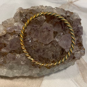 May include: A gold-toned twisted wire bangle bracelet. The bracelet is resting on a bed of amethyst crystals.