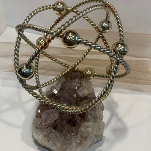 May include: A silver and copper wire sculpture with multiple spheres, resting on a large amethyst crystal cluster.
