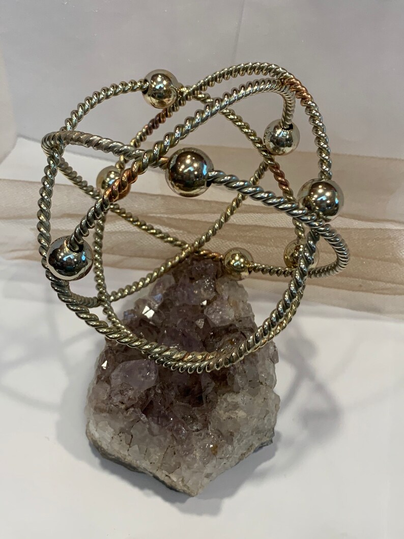 May include: A silver and copper wire sculpture with multiple spheres, resting on a large amethyst crystal cluster.