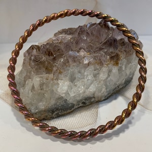 May include: A copper wire bracelet with a twisted design. The bracelet is a warm copper color with a hint of pink.