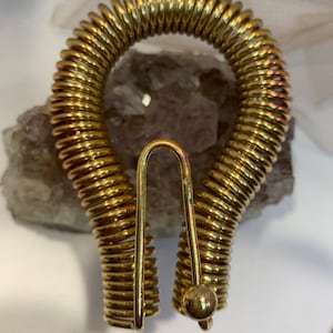 May include: A gold-colored metal spring coil keychain with a round ball at the end. The coil is in the shape of a horseshoe.