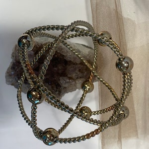 May include: Three silver bracelets with twisted rope designs and silver beads. The bracelets are intertwined and layered.