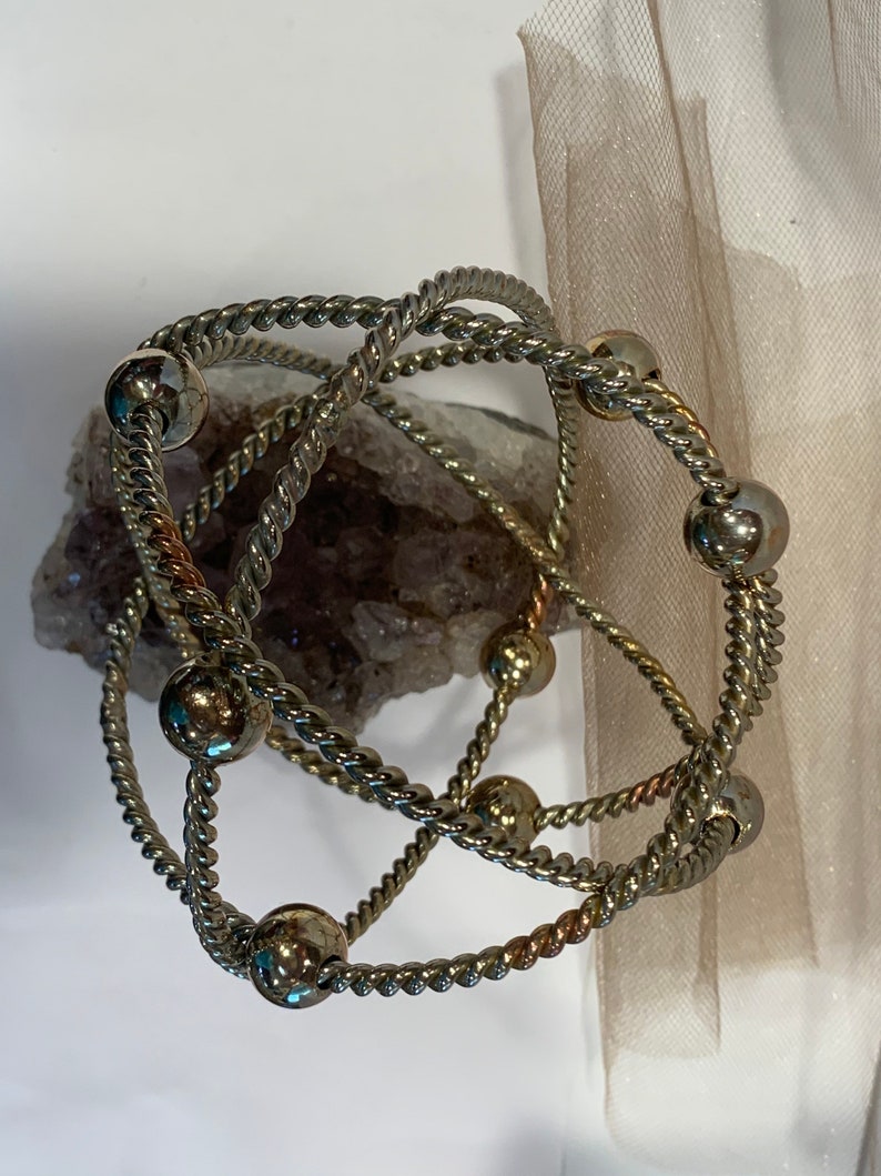 May include: Three silver bracelets with twisted rope designs and silver beads. The bracelets are intertwined and layered.