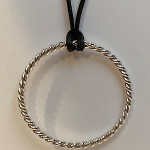 May include: A circular pendant featuring a twisted silver-toned metal design suspended from a thin black cord. The metallic ring has a continuous rope-like texture that catches the light, creating a reflective surface throughout the entire piece.