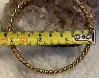 May include: A gold-colored twisted wire bangle bracelet measuring 2 inches in diameter.