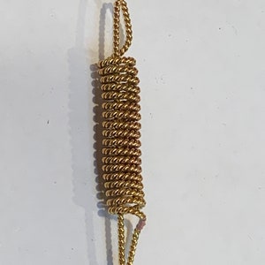 Puede incluir: Un muelle de metal de color dorado con un diseño retorcido. El muelle está enrollado y tiene dos bucles en los extremos.