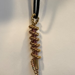 May include: A pendant necklace featuring a cylindrical, purple-toned rod wrapped in a spiral of gold-colored wire. The pendant hangs from a black cord. The wire has a twisted rope design.