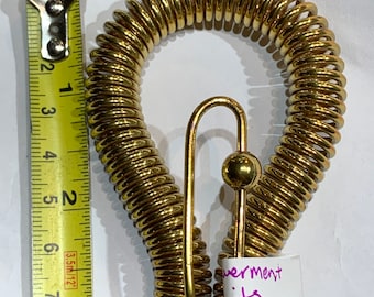 May include: A gold-colored metal spring coil with a hook and a ball at the end. The coil is about 7 inches long. The text "verment bits" is written on a white piece of paper.
