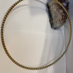 May include: A gold-colored, twisted metal hoop or ring. The hoop is lying on a white surface.