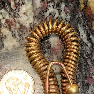 May include: A gold-colored metal coil spring with a hook on one end and a ball on the other end.