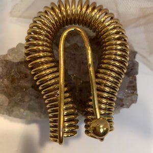 May include: A gold-colored metal coil ring with a rounded end. The coil is made of many small, tightly wound loops.