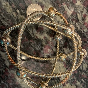 May include: Three silver bracelets with twisted rope designs and silver beads. The bracelets are layered on top of each other.