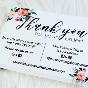 Op de afbeelding: Witte bedankkaart met een bloemrand. De kaart zegt "Bedankt voor uw bestelling!" en bevat een kortingscode, social media-handvatten en een website-adres.