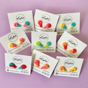 May include: Assortment of colourful candy-shaped earrings on white cards with the text "Kayla's Art Mart" and contact information. The earrings are in the shape of a teardrop and are made of polymer clay.