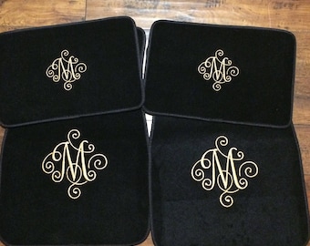 May include: Set of four black car floor mats with a gold embroidered monogram of the letter "M" on each mat.