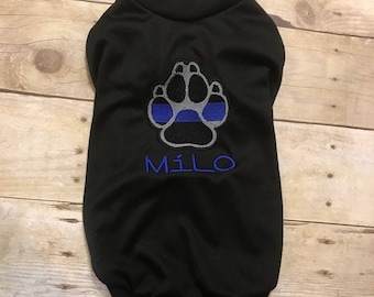May include: Black dog shirt with a blue line paw print and the name "MILO" embroidered on the front.