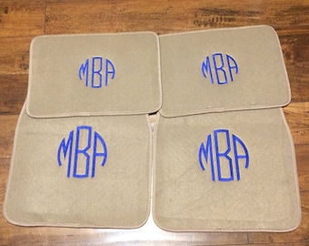 May include: Set of four beige car floor mats with blue embroidered initials "MBA" in a circle.