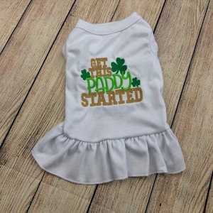 May include: White dog shirt with a gold and green embroidered design that says "Get this Paddy started" with shamrocks.