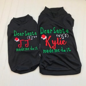 Puede incluir: Dos camisetas negras de Navidad con bordados verdes y rojos. La camiseta m&aacute;s grande dice "Querido Santa Kylie me hizo hacerlo" y la camiseta m&aacute;s peque&ntilde;a dice "Querido Santa JJ me hizo hacerlo".