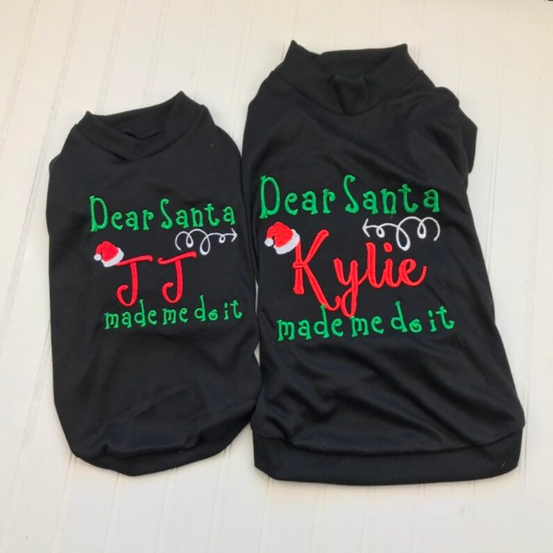 Puede incluir: Dos camisetas negras de Navidad con bordados verdes y rojos. La camiseta m&aacute;s grande dice "Querido Santa Kylie me hizo hacerlo" y la camiseta m&aacute;s peque&ntilde;a dice "Querido Santa JJ me hizo hacerlo".