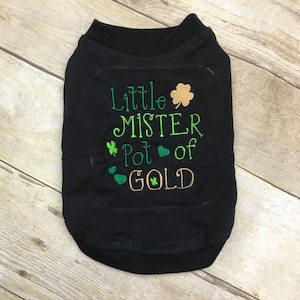 Peut inclure: T-shirt noir pour chien avec des trèfles verts et une broderie dorée qui dit "Little Mister Pot of Gold".