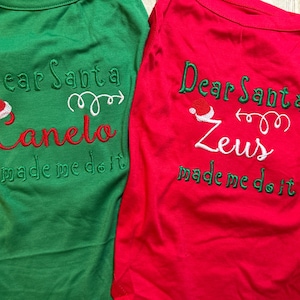 Puede incluir: Dos camisetas para perros rojas y verdes con el texto "Querido Santa [nombre del perro] me hizo hacerlo" y un gr&aacute;fico de gorro de Pap&aacute; Noel. Las camisetas son para Canelo y Zeus.
