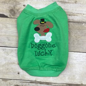May include: Green dog shirt with a cartoon dog wearing a green hat and holding a bone. The shirt says "doggone lucky".