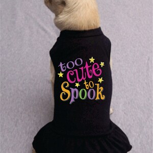 May include: A black dog dress with a ruffle hem and the text "too cute to spook" in colorful letters with yellow stars.