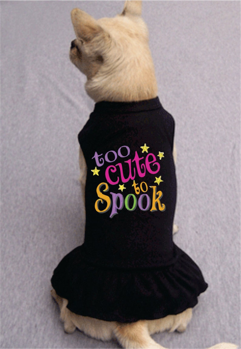 May include: A black dog dress with a ruffle hem and the text "too cute to spook" in colorful letters with yellow stars.