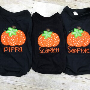 Peut inclure: Trois t-shirts noirs avec des motifs de citrouille orange et blanche et les noms "Pippa", "Scarlett" et "Sophie" brod&eacute;s dessus.
