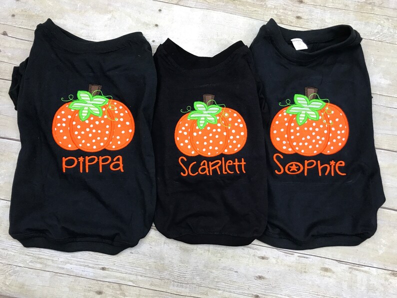 Peut inclure: Trois t-shirts noirs avec des motifs de citrouille orange et blanche et les noms "Pippa", "Scarlett" et "Sophie" brod&eacute;s dessus.