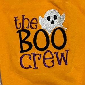 May include: A yellow shirt with the text "the BOO crew" embroidered in black and purple thread. A white ghost with black eyes and a mouth is embroidered above the text.