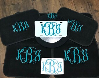 May include: A set of six black car floor mats with a teal monogram "KBB" embroidered on each mat. The set also includes a teal monogram "KBB" license plate frame and a teal monogram "KBB" sticker.