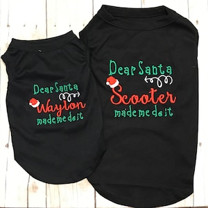 Puede incluir: Dos camisetas negras para perros con bordados verdes y rojos. La camiseta m&aacute;s grande dice "Querido Santa Scooter me hizo hacerlo" y la camiseta m&aacute;s peque&ntilde;a dice "Querido Santa Waylon me hizo hacerlo".