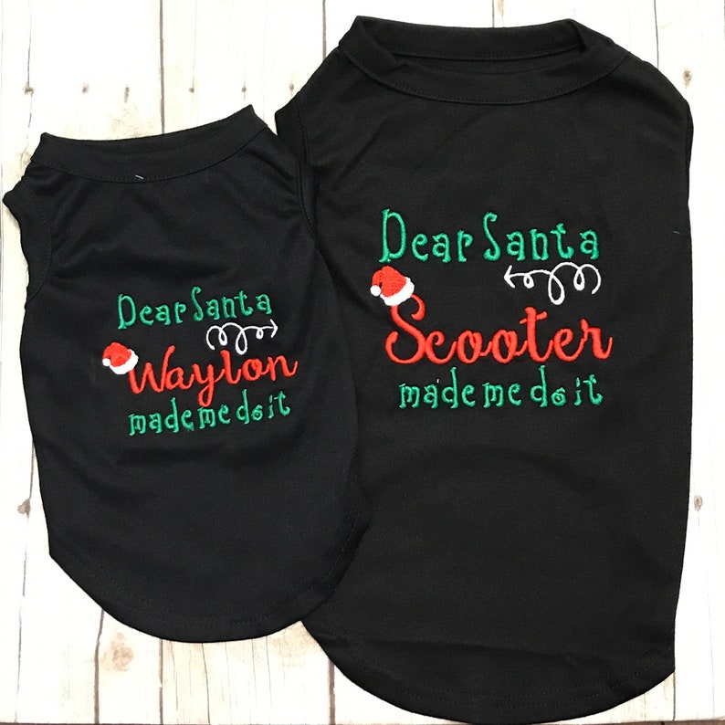 Puede incluir: Dos camisetas negras para perros con bordados verdes y rojos. La camiseta m&aacute;s grande dice "Querido Santa Scooter me hizo hacerlo" y la camiseta m&aacute;s peque&ntilde;a dice "Querido Santa Waylon me hizo hacerlo".