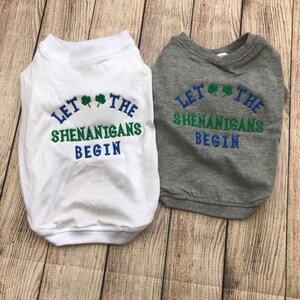 May include: Two dog shirts with the text "Let the Shenanigans Begin" and shamrock designs. One shirt is white and the other is gray.