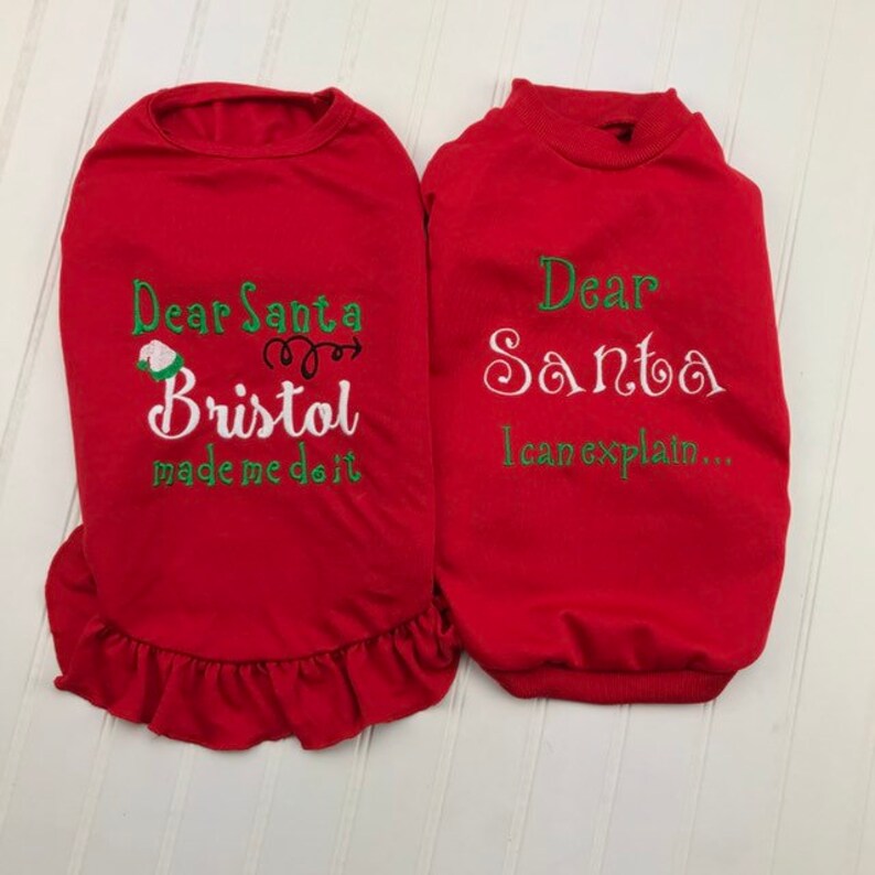 Puede incluir: Dos su&eacute;teres rojos para perro con mensajes navide&ntilde;os bordados. El primer su&eacute;ter dice "Querido Santa Bristol me hizo hacerlo" con un gorro de elfo verde y una flecha. El segundo su&eacute;ter dice "Querido Santa Puedo explicarlo..."