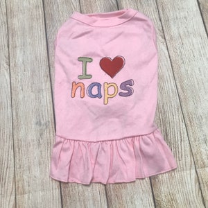 May include: Pink dog shirt with a ruffled hem and embroidered text that says "I love naps" with a red heart.