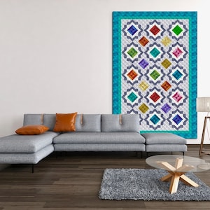May include: A gray sectional sofa with two orange throw pillows in front of a white wall with a colorful geometric patterned wall hanging.