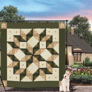 May include: A green, beige, and white quilt with a log cabin pattern. The quilt is hanging on a stand in front of a house.