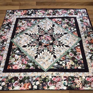Puede incluir: Una colcha con un patrón floral en tonos de rosa, verde y marrón. La colcha presenta un diseño de estrella en el centro y un borde de tela floral.