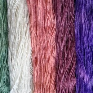 May include: Close-up of seven skeins of yarn in various colors, including green, white, pink, purple, blue, and a darker blue. The yarn is arranged vertically, with each skein showing its texture and color.