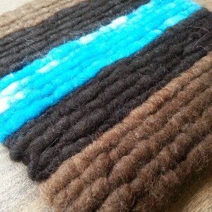 May include: A close-up of a woven rug with brown, black, and turquoise stripes. The rug is made of wool and has a soft, textured surface.