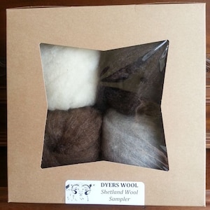 May include: A cardboard box with a clear window showing four balls of Shetland wool in white, brown, gray, and black. The box has a label that reads "Dyers Wool Shetland Wool Sampler".